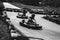 Grayscale closeup shot of a person karting on a go-kart track surrounded by wheels, on a sunny day