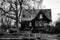 Grayscale dramatic shot of an old abandoned house with dry and dead plants on its lawn