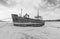 Grayscale of a ferry side abandoned wales boat on the sandy beach, cloudy sky background