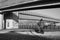 Grayscale shot of a child cycling under the bridge by the river