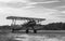 Grayscale shot of a classic propeller plane landing on the runway with greenery around it