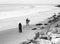 Grayscale shot of a couple and a surfer on the shore of a beach