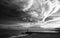 Grayscale shot of a person standing on the rocks on the seaside on a cloudy day