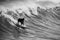 Grayscale shot of a surfer catching a wave in the rolling ocean