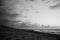 Grayscale shot of waves crashing on beach under the cloudy sky