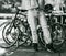 Grayscale shot of a woman leaning against bicycles