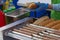 Greasy hot dog sausages on a culinary machine in a cafe. Cooking sausages for a hot dog bun with sesame seeds in the background.