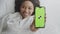 Great mobile app. Positive african american woman showing smartphone with green chroma key screen, lying in bed