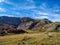 Great mountain range found in distant natural serene environment with blue skies above and green grass field on the ground