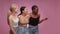 Great shopping promo. Three diverse women looking aside and laughing at empty space, smiling to camera, pink background