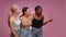 Great shopping promo. Three diverse women looking aside and laughing at empty space, smiling to camera, pink background