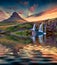 Great sunrise on Kirkjufellsfoss Waterfall reflected in calm waters of Atlantic ocean.