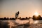 Great view of dark silhouette of active male rider holds rope and making extreme jump on wakeboard at sunset.