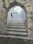 Greece, Tinos island, Cyclades. Arched stonewall entrance in front of stone paved stairs. Vertical