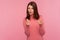 Greedy mercantile woman with brown hair in pink sweater asking cash showing money gesture with fingers seriously looking at camera