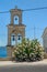 Greek belfry near the church with a large azalea bush by the road