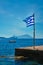 Greek flag in the blue sky on pier and traditional greek fishing boat in the Aegean sea