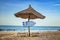 Greek flag on wooden arrow sign. There are two sun loungers and a sun umbrella on the beach. It is a tropical paradise with a