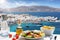 Greek food with salad, feta cheese and olive oil served with a view to the island of Mykonos, Greece