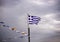 Greek national flag on flagpole and some other small flags waving against a dramatic blue sky
