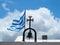 The Greek National flag near cross of small church against blue