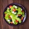 Greek salad (lettuce, tomatoes, feta cheese, cucumbers, black olives) on dark wooden background