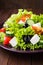 Greek salad (lettuce, tomatoes, feta cheese, cucumbers, black olives) on dark wooden background close up