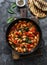 Greek style tomato sauce, spinach, paprika, beans stew in a cast iron pan on a rustic board on a dark background, top view. Simple