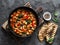 Greek style tomato sauce, spinach, paprika, beans stew in a cast iron pan on a rustic board on a dark background, top view. Simple