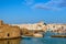 Greek whitewashed houses, old castle and church by harbour waterfront on sunny day, Naoussa, Paros island, Greece