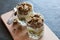 Greek yogurt, granola, banana and kiwi. Desserts in glass cups with spoons on wooden platform, dark background, view from the top