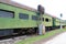 Green abandoned passenger train cars with boarded windows beside light posts on train tracks