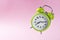 Green alarm clock with two bells showing ten minutes past seven on the pink background