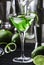 Green alcoholic cocktail martini glass with dry gin, vermouth, liquor, lime zest and ice, bar tools, dark background