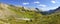 Green Alpine Meadow Wide Panoramic Landscape with Rugged Rocky Mountain Peaks and Blue Sky on Horizon