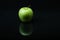 Green apple on a black background with reflection.