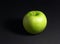 Green apple on black background with small shadow