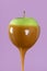 Green apple with caramel sauce close-up minimalist on purple background