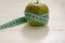 Green apple wrapped in centimeter on white wooden background wit