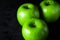 Green apples on a black background. Three apples stand next to each other.