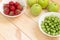 Green apples, gooseberry and red strawberries in white bowles on light wooden table