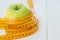 Green apples with measuring tape on white wooden background. Dieting concept