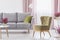 Green armchair standing in white living room interior with grey couch, window with pastel pink drapes and heathers