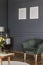 Green armchair and wooden cupboard standing against black wall w