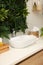 Green artificial plants, vessel sink and different personal care products in bathroom