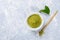 Green asian matcha tea powder in white bowl, special wooden bamboo spoon and fresh leaves on grey textured background.