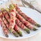 Green asparagus wrapped with bacon on white plate, square format