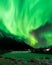 Green aurora borealis lighting the night sky above an open grassy field.