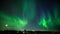 Green aurora northern light dancing under a starry and moonlit sky on a frozen lake in a nordic country