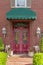 Green awning over a beautiful red door with decorative wrought iron gate